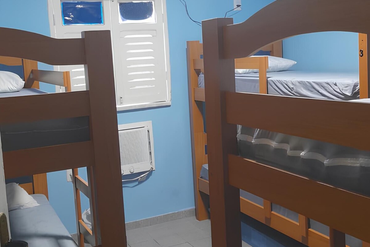 A dormitory room with bunk beds, a ceiling fan, a window, and a wall-mounted heater.