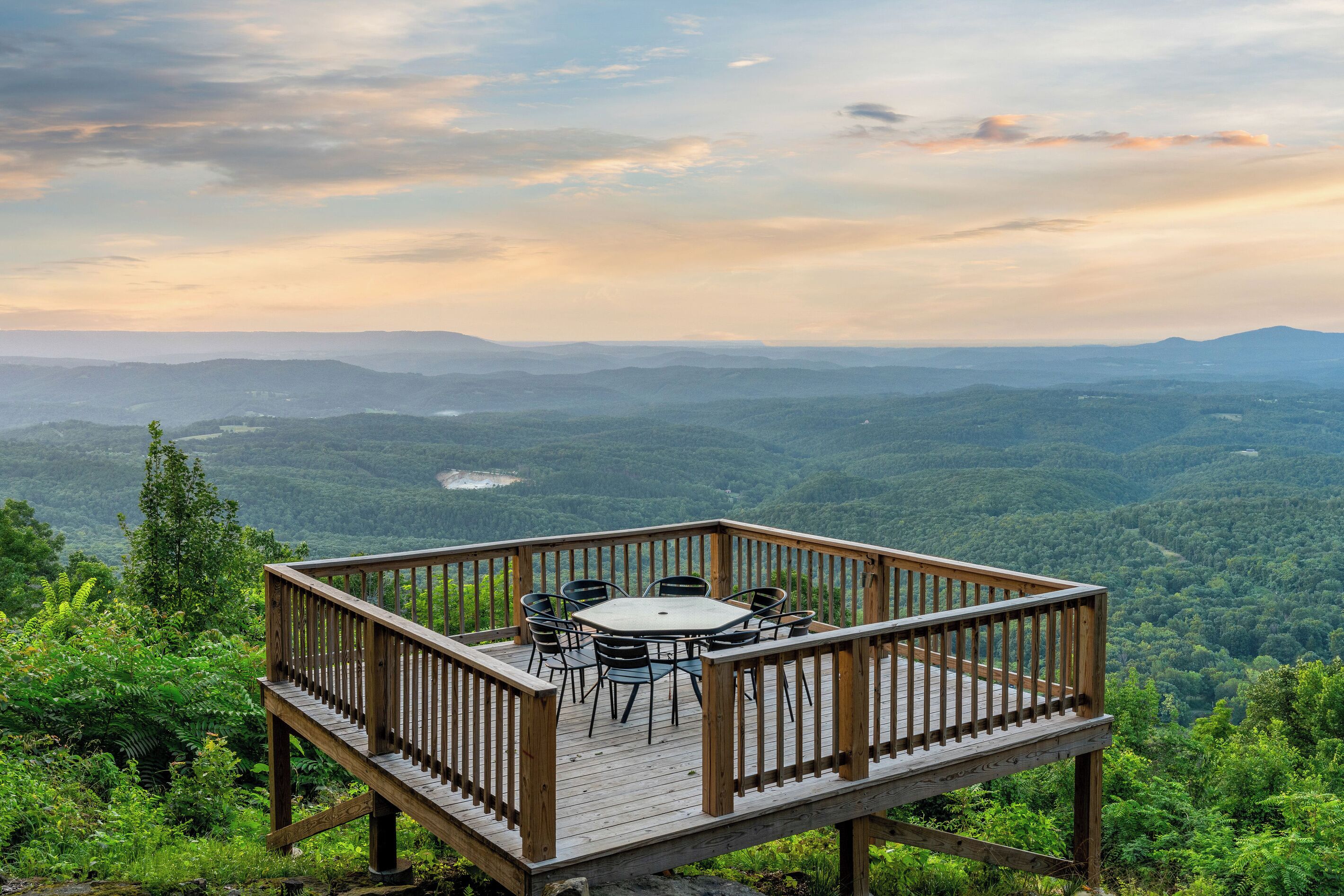 A wooden deck with a table and chairs overlooking a forested valley.