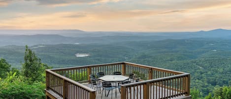 A wooden deck with a table and chairs overlooking a forested valley.