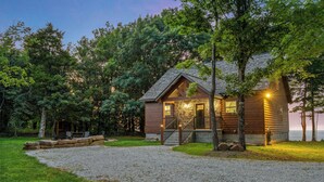A cabin with a stone foundation, wooden exterior, and a gravel driveway.