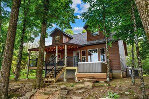 A wooden cabin with a deck, stairs, and a hot tub.