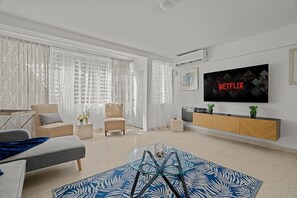 A modern living room with a sofa, armchairs, a coffee table, and a TV mounted on the wall. - Ocean Park 2BR Backyard BBQ Walk to Beach (San Juan)