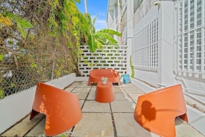 Eine Dachterrasse mit orangefarbenen Stühlen und einem kleinen Tisch, umgeben von einem weißen Zaun und üppiger Bepflanzung.