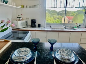 A kitchen with a stove, microwave, coffee maker, and a window with a view of greenery. - Tropical Tamarindo Condo; 5-Min Walk to Beach (Tamarindo)