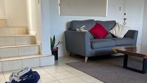 A living room with a grey sofa, a coffee table, a staircase, and a basket of folded towels.