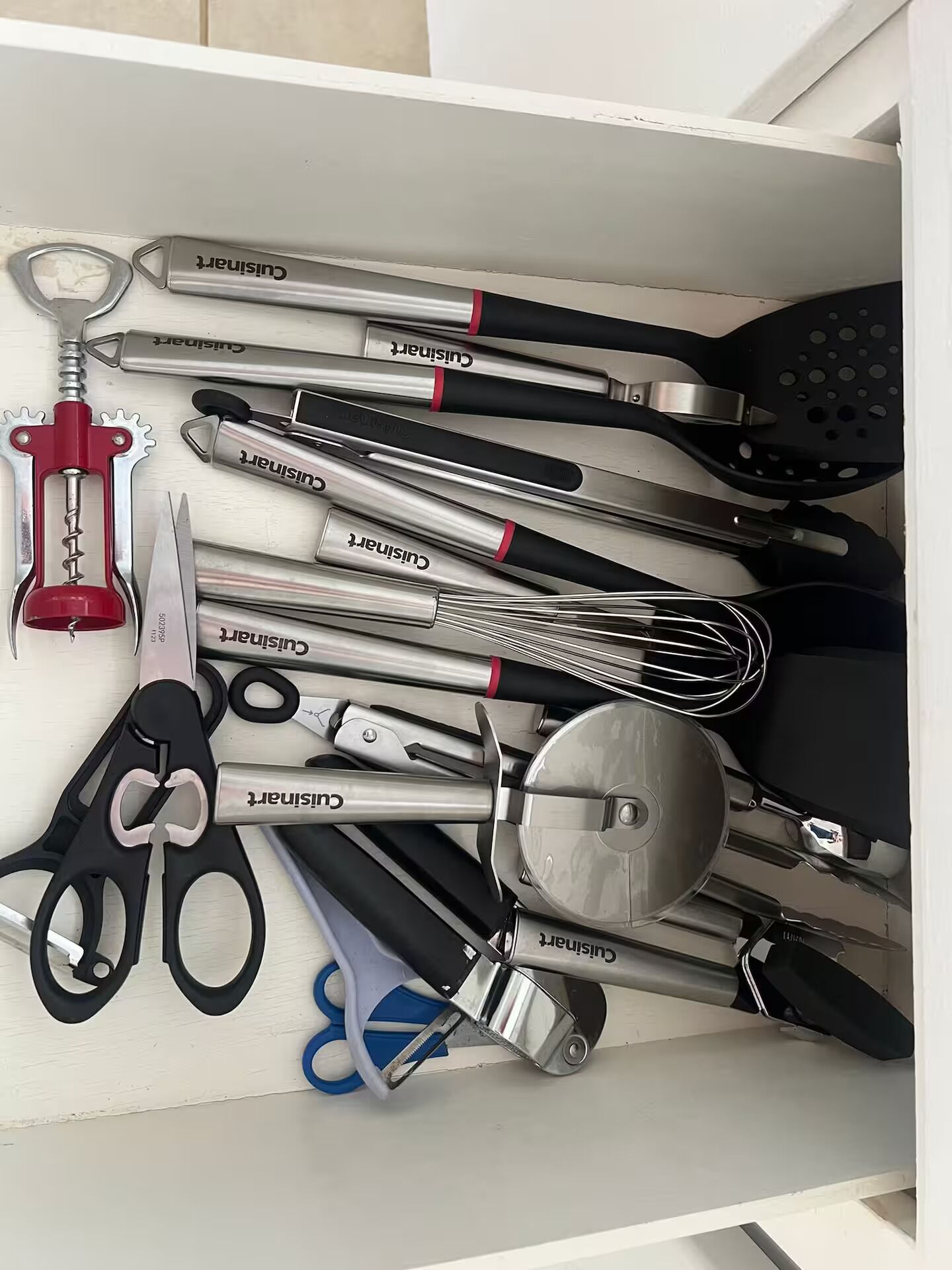 Een lade gevuld met verschillende keukengereedschappen, zoals een schaar, een garde en een flesopener.