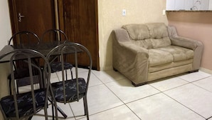 Ein Zimmer mit Esstisch und Stühlen, einer Couch, einer Holztür und einem Fliesenboden.