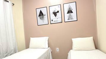 Quarto com duas camas, uma cortina branca e três quadros na parede.