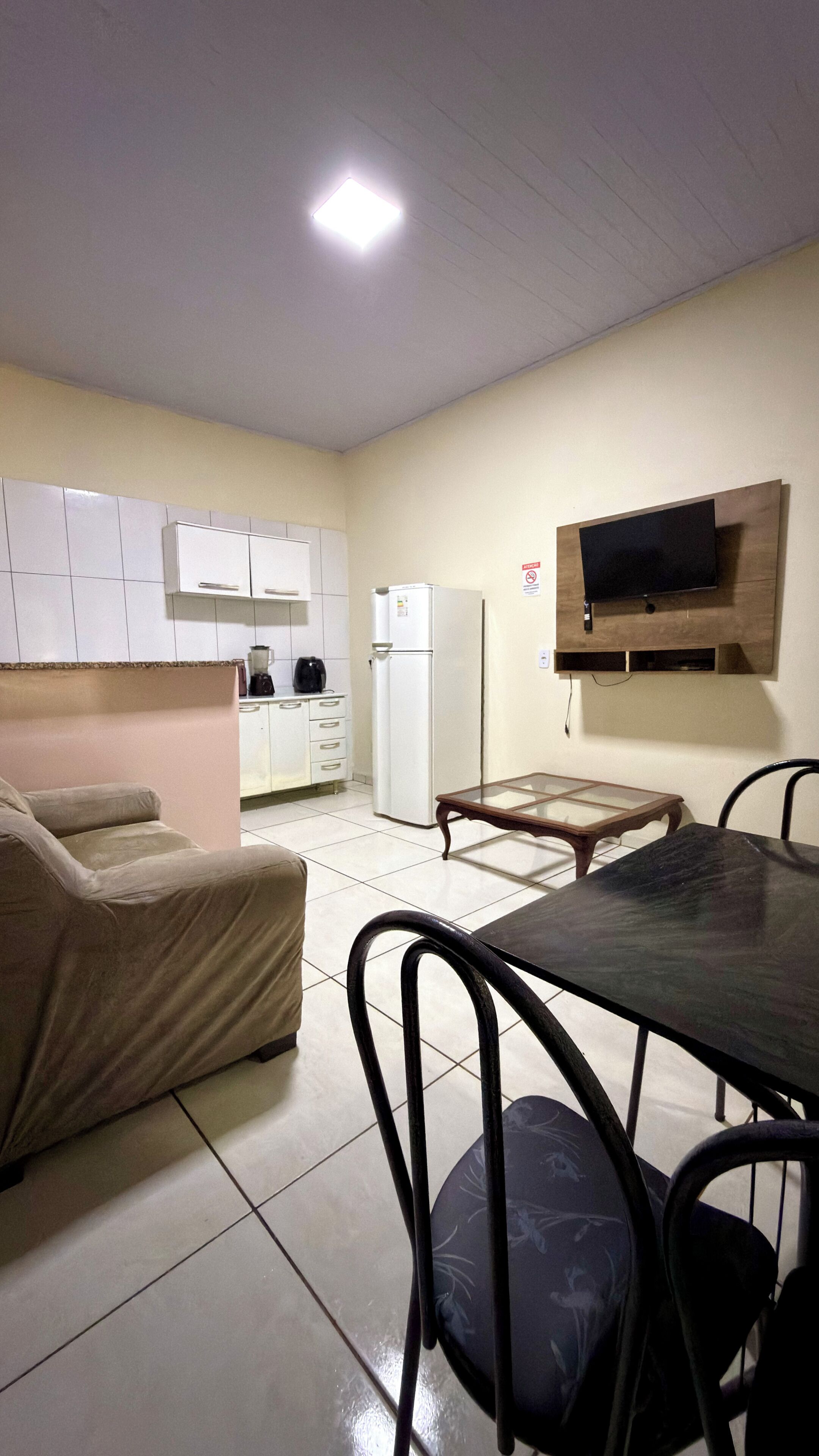 Un espacio habitable compacto con kitchenette, un sofá, una mesa de comedor con sillas y un televisor de pantalla plana montado en la pared.