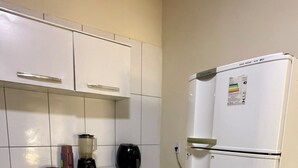 Eine kleine Küche mit weißen Schränken, einem Kühlschrank, einer Arbeitsplatte mit Mixer und Wasserkocher sowie einem Fliesenboden.