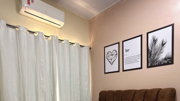 Ein Schlafzimmer mit einem Bett, weißen Vorhängen, einem braunen Kopfteil und zwei gerahmten Bildern an der Wand.