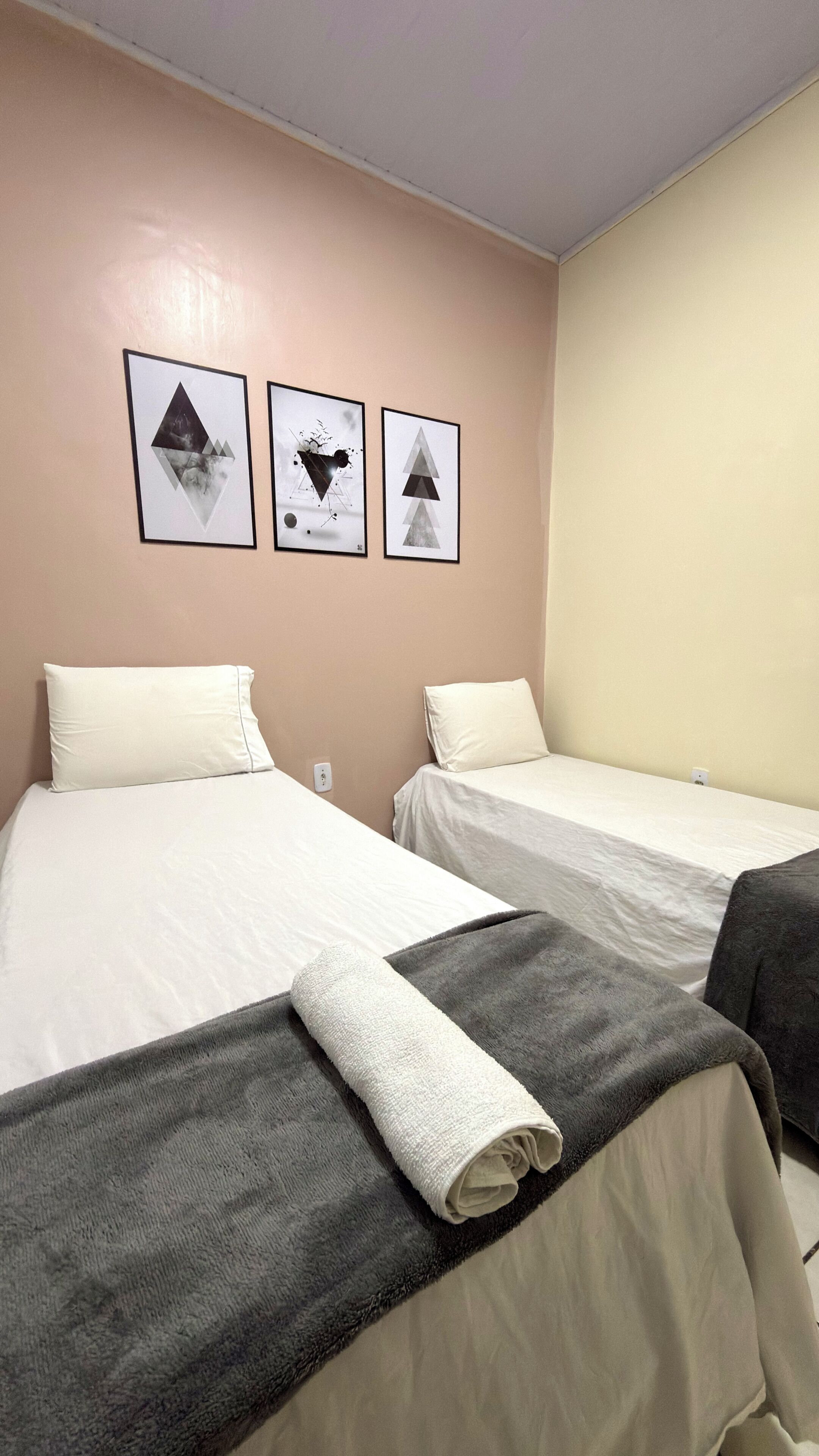 A hotel room with two beds, a beige wall, and three framed pictures.