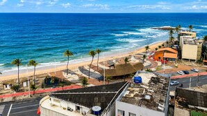 A coastal view with a beach, palm trees, and buildings. - Apartment with ocean view in Smart Pituba. (Salvador)