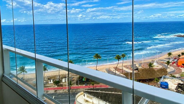 A view of the ocean from a window with a balcony railing. - Apartment with ocean view in Smart Pituba. (Salvador)