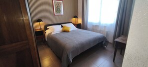 Ein Schlafzimmer mit Bett, Nachttischlampen, einem Nachttisch, einem gerahmten Bild an der Wand und einem Fenster mit Vorhängen.