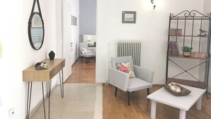 Ein Zimmer mit einem Sessel, einem kleinen Tisch, einer Heizung, einem Bücherregal und einem Spiegel.