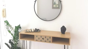 Ein schlicht eingerichteter Raum mit einem Holzkonsolentisch, einem wandmontierten, ovalen Spiegel, einer kleinen Buddha-Statue und einer Topfpflanze.