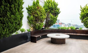 Una terraza en la azotea con una mesa redonda de piedra, zona de estar y plantas en macetas.