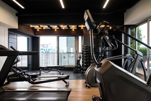 Une salle de sport équipée de tapis de course, d’un rameur et d’un banc de musculation.