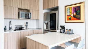 Eine moderne Küche mit Holzschränken, einer Mikrowelle, einem Kühlschrank, einer Kaffeemaschine und einem gerahmten Gemälde.