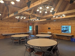 A wooden cabin interior with round tables, chairs, and a ceiling with exposed beams and lights.