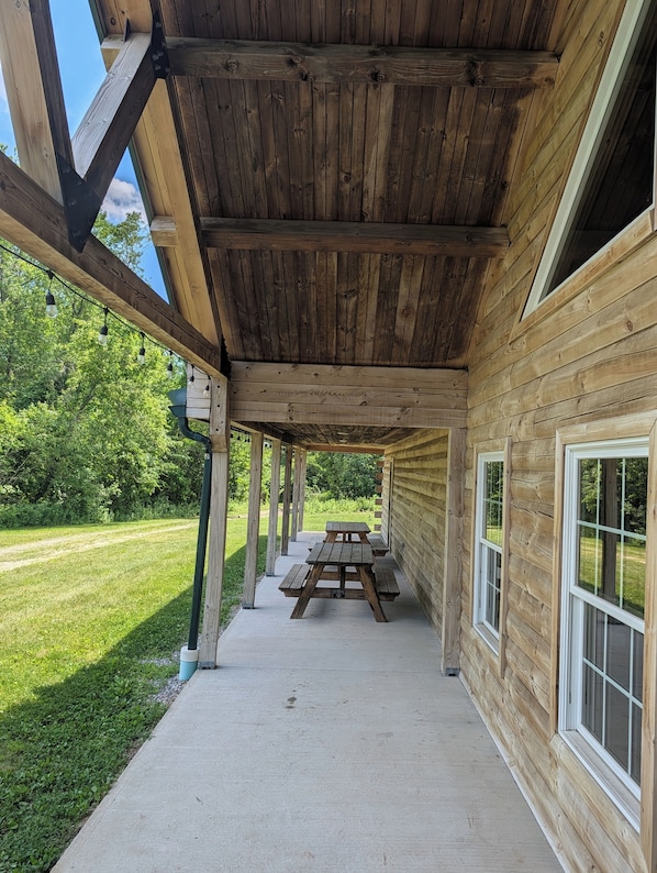 A covered outdoor area with a picnic table, wooden beams, and a grassy landscape.