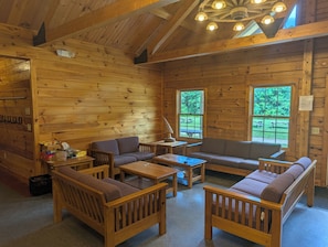 A cabin interior with wooden walls, a ceiling fan, a sofa, a table, and two windows.