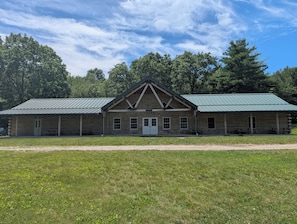A log cabin with a green metal roof, a central entrance, and a porch with benches.
