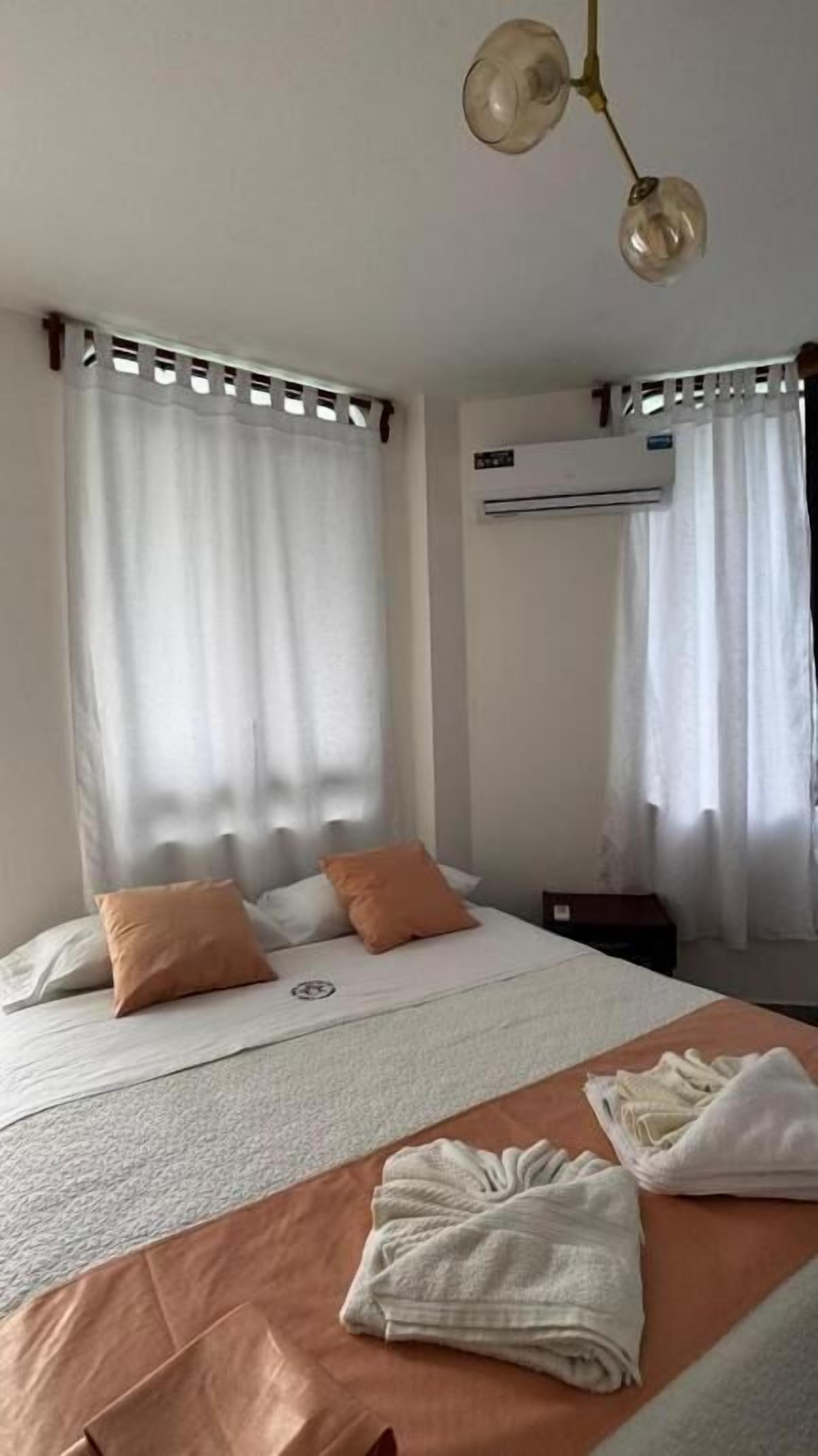 Ein Hotelzimmer mit einem Bett, zwei Kissen, einer Decke, einem Handtuch, einer Klimaanlage und einer Deckenleuchte.