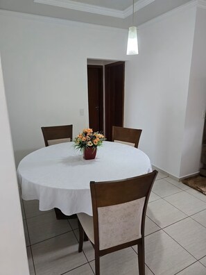 Una mesa redonda para comer con mantel blanco, cuatro sillas de madera y un florero con flores.