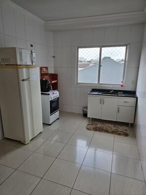 Cocina compacta con armarios blancos, refrigerador, microondas, horno y ventana con vista.