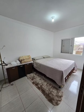 A bedroom with a bed, a dresser, a mirror, a window with blinds, and a ceiling light.