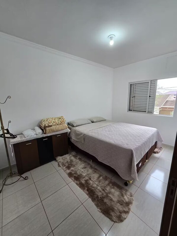 A bedroom with a bed, a dresser, a mirror, a window with blinds, and a ceiling light.