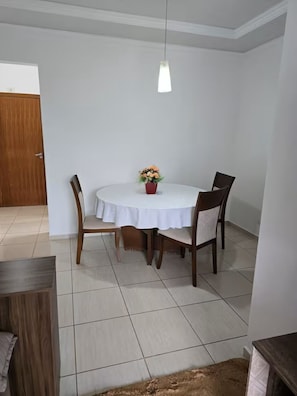 Comedor con una mesa redonda, cuatro sillas, una planta en maceta y una lámpara colgante.