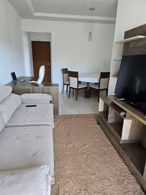 Una habitación de hotel moderna con una cama, un escritorio con una computadora portátil, una mesa de comedor con sillas y un televisor sobre un soporte de madera.