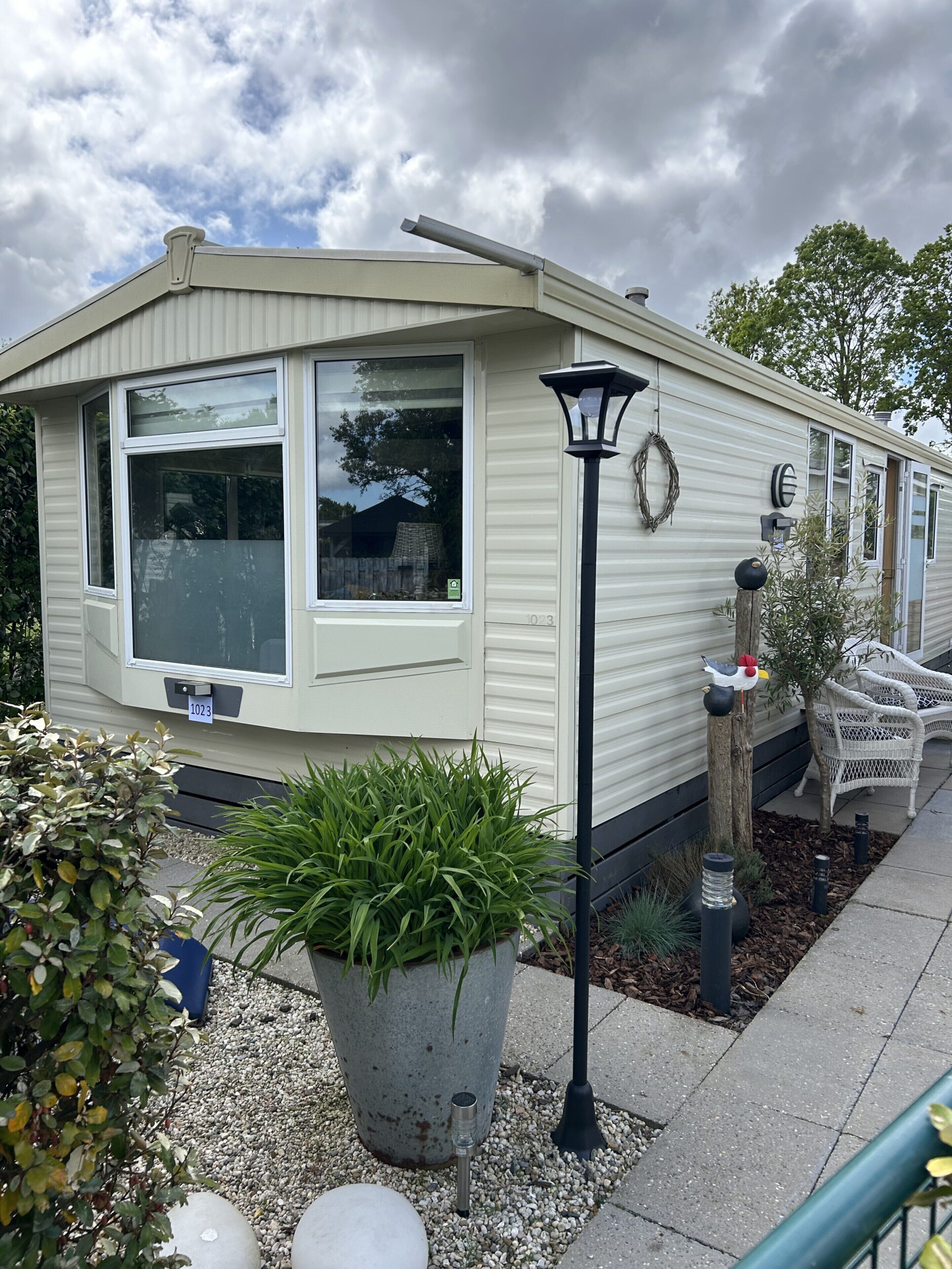 A mobile home with a large window, a potted plant, and a street lamp.