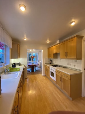 A kitchen with wooden cabinets, a sink, a stove, and a dining area in the background. - Spacious Family Residence with large south facing gardens close to Eden Project (St Austell)