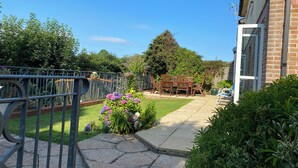Ein wohnlicher Garten mit Terrasse, einem Holztisch und -stühlen sowie einem Metallzaun.