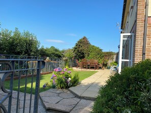A residential garden with a patio, a wooden table and chairs, and a metal fence. - Spacious Family Residence with large south facing gardens close to Eden Project (St Austell)