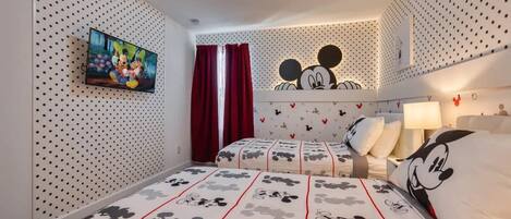 Een slaapkamer met een Mickey Mouse beddeken, een televisie aan de muur en een plafondlamp.
