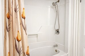Une salle de bain avec une baignoire, une douche et un rideau de douche orné d’un motif de feuilles.