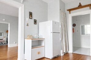 Une pièce avec un réfrigérateur blanc, un meuble en bois, un miroir et une fenêtre avec des rideaux.