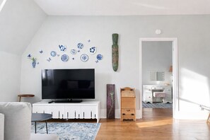 A living room with a flat-screen TV, a white cabinet, a small wooden table, and a blue patterned rug. - Village Heritage Suite with Full Kitchen & King Bed (Merrickville)