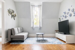 Un salon avec un canapé, une petite table ronde, un téléviseur et des assiettes décoratives accrochées au mur.