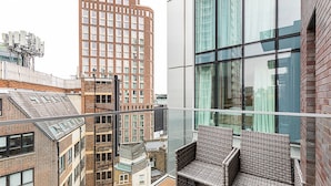 En høj bygning med en glasbalkon, flet møbler og udsigt til andre bygninger.