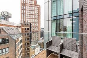Ein Hochhaus mit einem Glasbalkon, Korbmöbeln und Blick auf andere Gebäude.