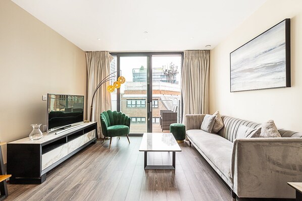 Ein modernes Wohnzimmer mit Flachbildfernseher, einem grünen Sessel, einem grauen Sofa und einem Couchtisch.