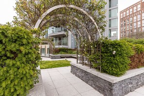 Ein modernes Gebäude mit einem Steinweg, Grünflächen und einem Metallbogen.