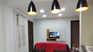 Ein Essbereich mit schwarzer Arbeitsplatte, drei Pendelleuchten, einem an der Wand montierten Fernseher und einer roten Tischdecke.