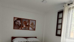 Ein Zimmer mit einem Bett, einem fensterbelaubten Fenster und drei gerahmten Bildern an der Wand.